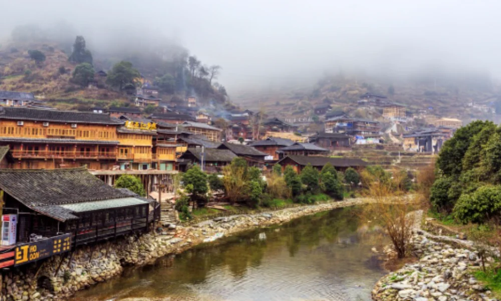 Foggy village on a hillside with traditional wooden buildings by a river