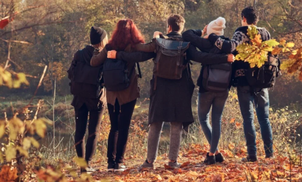 Five friends stand arm-in-arm on a leaf-covered path-good travel destinations in october