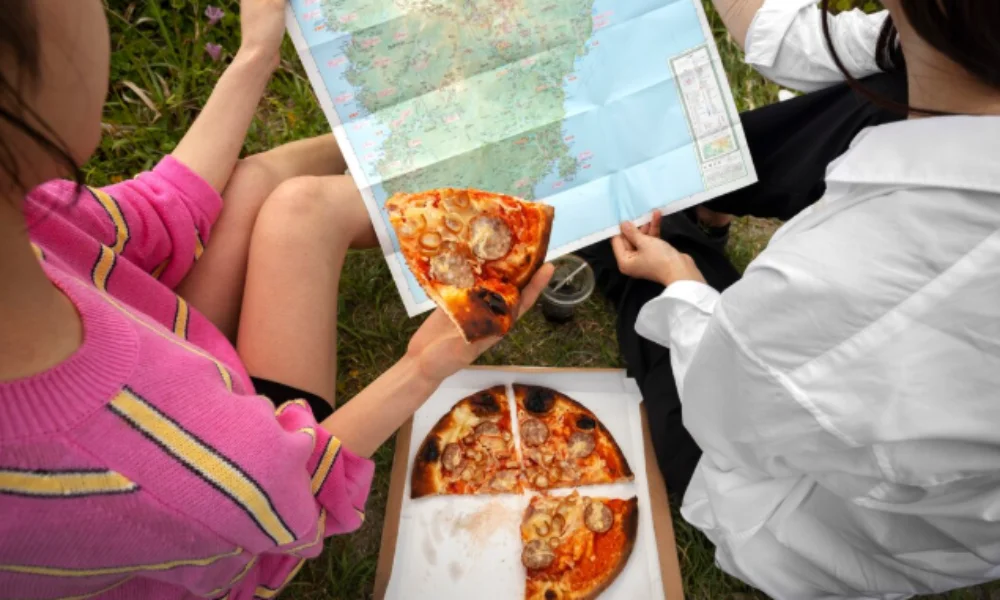 Two individuals on the grass, looking at a map and sharing a pizza