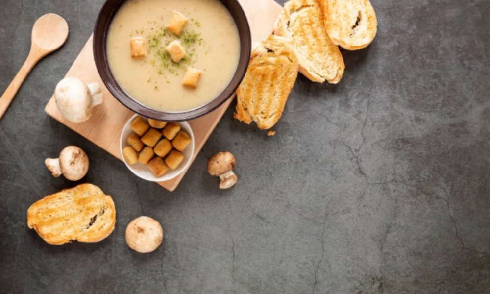 A bowl of creamy mushroom soup topped with croutons sits on a wooden board-potato soup recipe