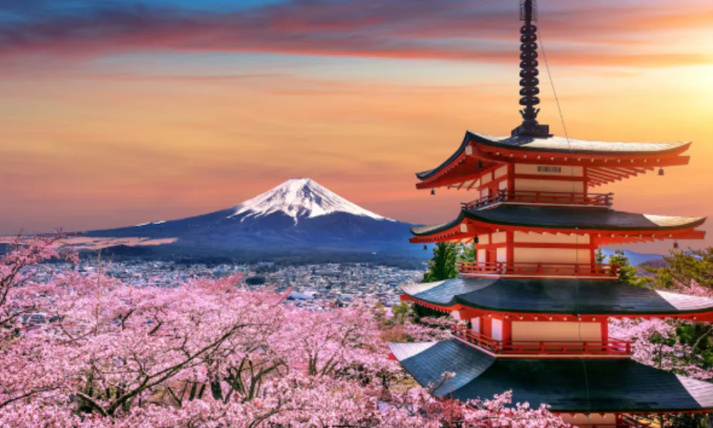 A serene scene of Mount Fuji at sunset with a foreground of a traditional Japanese pagoda and blooming cherry blossoms