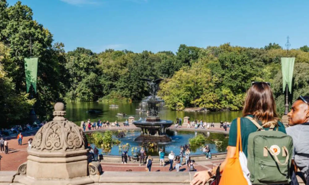 Tourists at a stone balcony overlook a sunlit park featuring a fountain