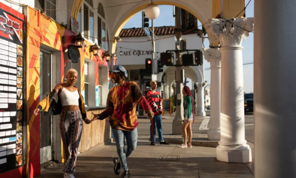 Two people walk hand in hand under arched walkways with vibrant murals and columns