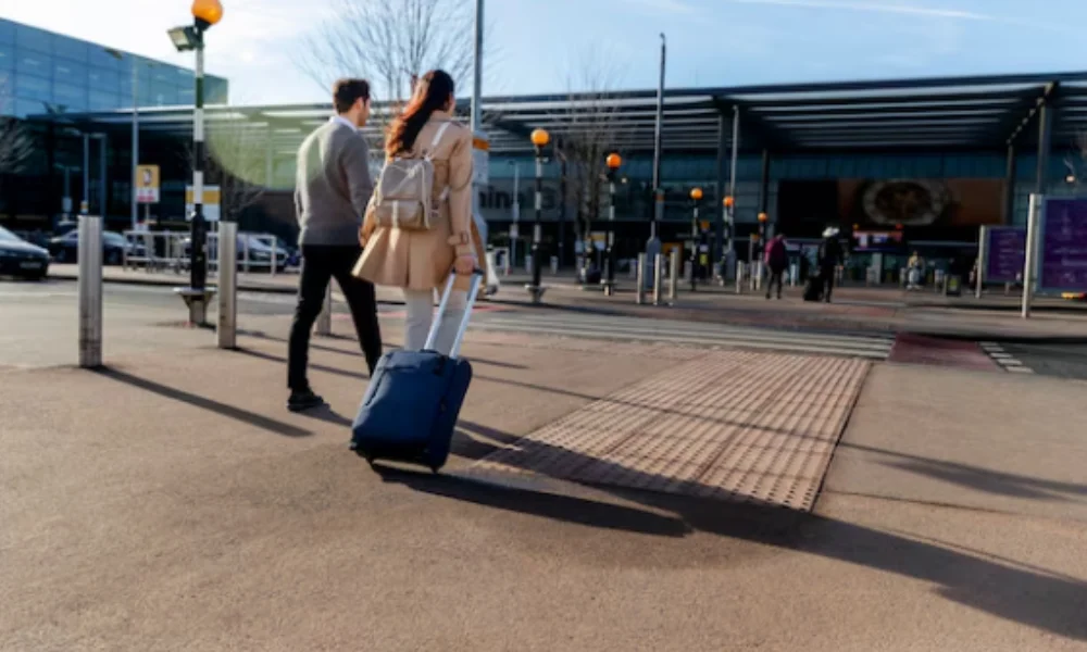 A couple walking towards an airport terminal, pulling a blue suitcase-planning a trip to new york