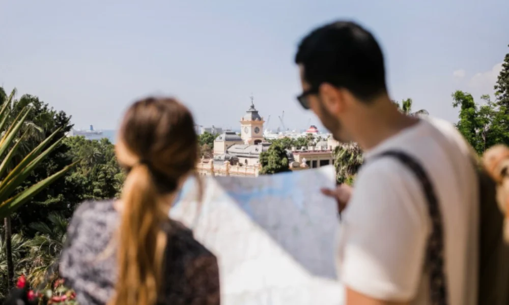 A man and woman holding a map stand facing a distant cityscape with a prominent clock tower