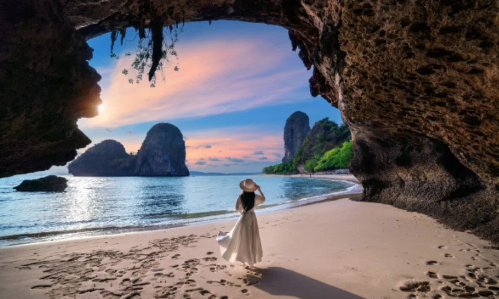 A woman in a white dress and hat stands on a sandy beach-good asian countries to visit