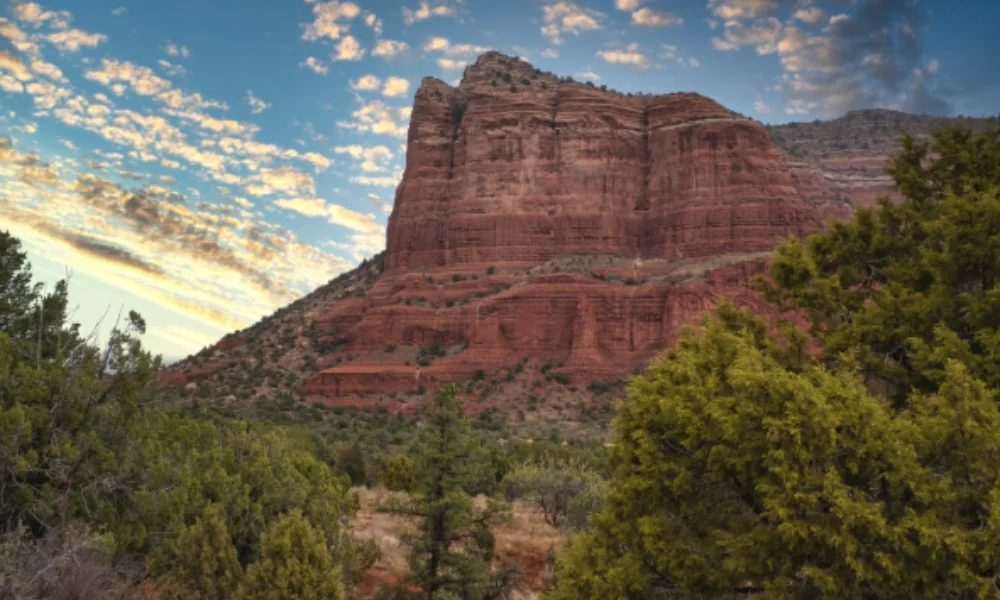 A majestic red rock formation towers over a landscape of green trees
