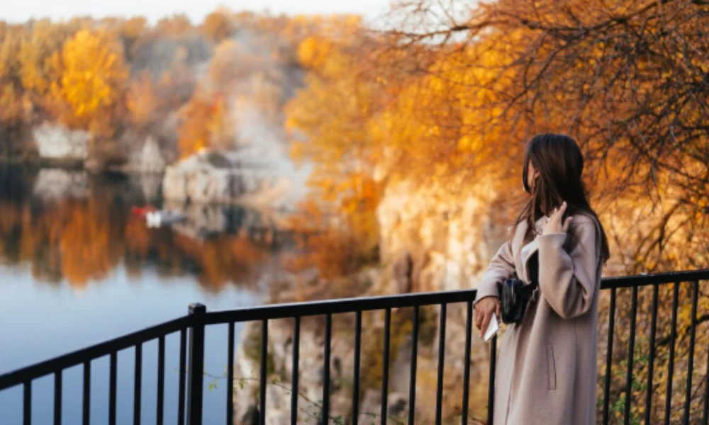 A woman in a beige coat stands by a black railing-good travel destinations in october