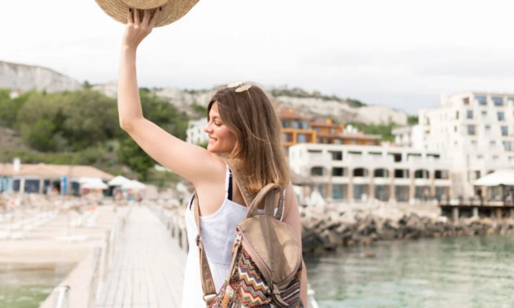 A woman wearing a hat and backpack stands on a wooden pier