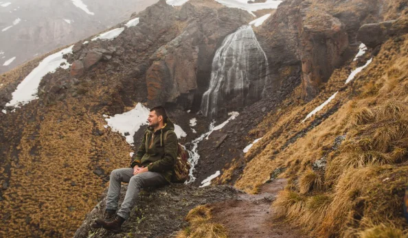 A man in a green jacket and backpack sits on a cliff-south america travel destinations