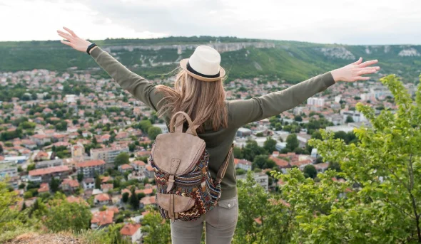 Woman with a backpack and hat stands on a hilltop