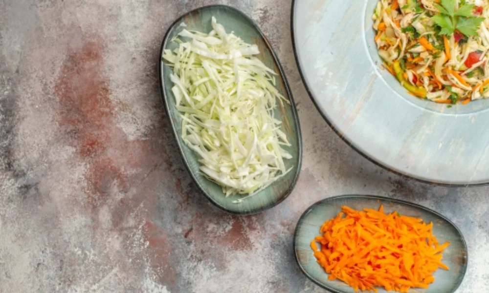 Shredded cabbage and carrots on oval plates next to a bowl of colorful salad on a textured-easy coleslaw recipe