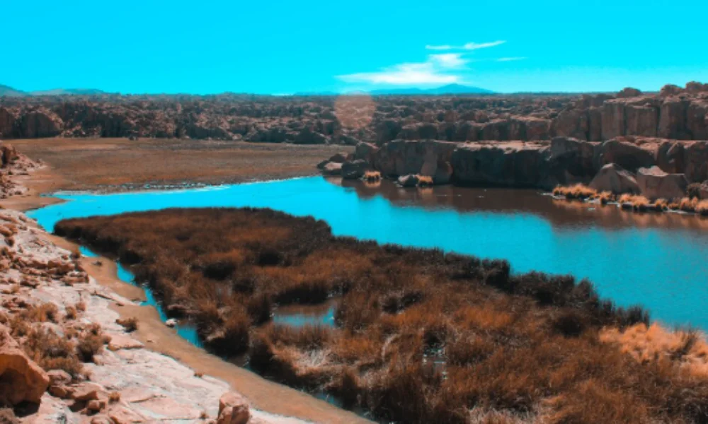 A serene desert landscape features a calm river meandering through rocky terrain