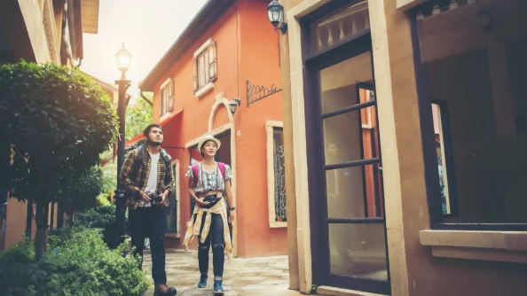 Two people stroll through a charming street with orange buildings and greenery-east coast travel destinations