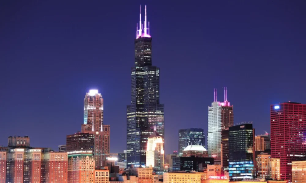 Chicago skyline at night with the Willis Tower prominently lit in pink against a dark blue sky