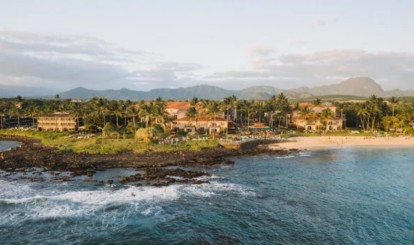 Coastal resort with red-roofed buildings and palm trees, set against a backdrop of mountains