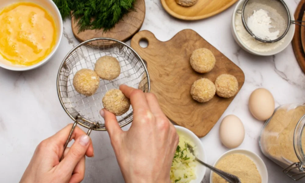 Hands holding a wire basket with breaded balls above a wooden board on a kitchen counter-easy cheeseball recipes