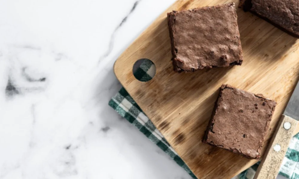 Three brownies on a wooden cutting board sit atop-easy fudge recipes