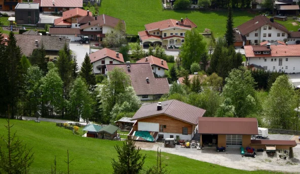 A quaint village with houses featuring red and brown roofs nestled among lush green trees and grassy hills