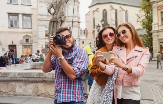A cheerful outdoor scene with three friends in a lively square. Two women take a selfie-travel destinations in europe