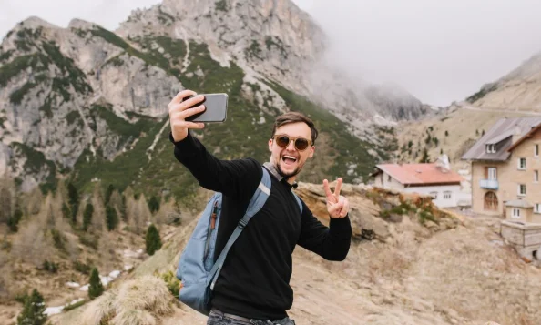 A man wearing sunglasses and a black sweater takes a selfie on a mountain trail-cheap travel destinations in Europe