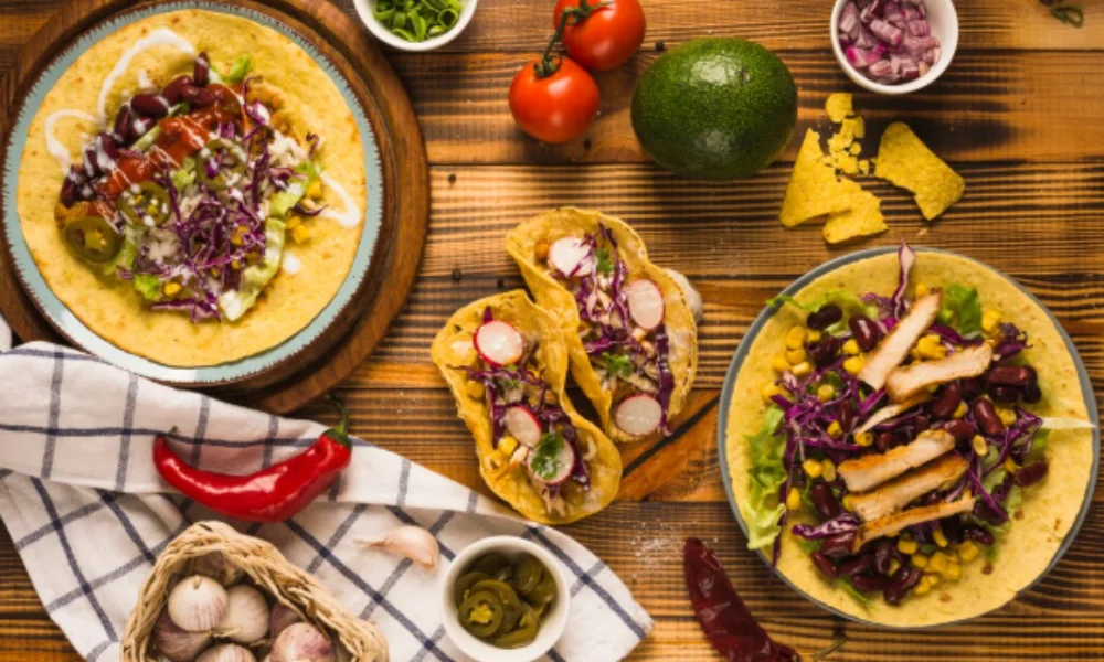 A wooden table filled with vibrant tacos: one open with beans
