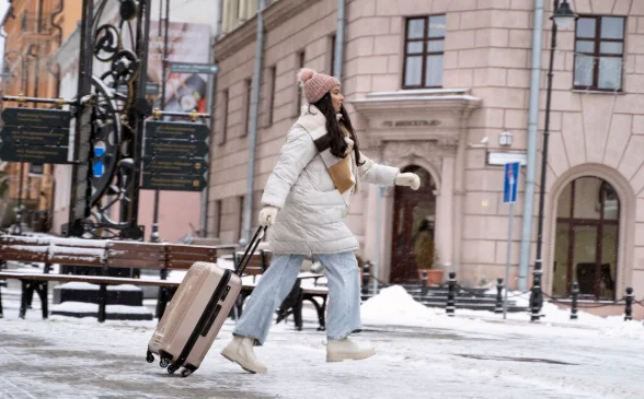 A woman in a white coat and pink hat walks on a snowy street-Cheap Destinations to Travel in December