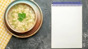 A bowl of creamy soup garnished with herbs sits on a patterned napkin