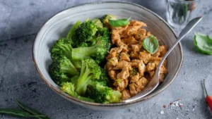 A ceramic bowl filled with vibrant green broccoli and spiced crumbled tofu. A spoon rests inside
