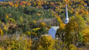 A white church with a tall steeple is nestled among vibrant autumn foliage in shades of orange