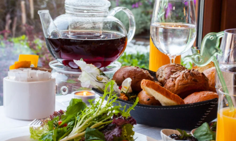 A table set with a glass teapot of dark tea, a bowl of assorted breads, fresh salad greens-Places to Visit in Vermont
