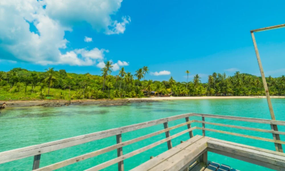 A scenic beach view from a wooden deck overlooking clear turquoise waters