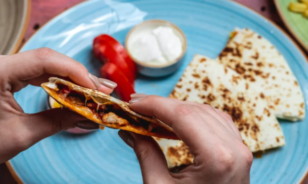 Two hands hold a quesadilla with a melted cheese and vegetable filling-easy birria tacos recipe