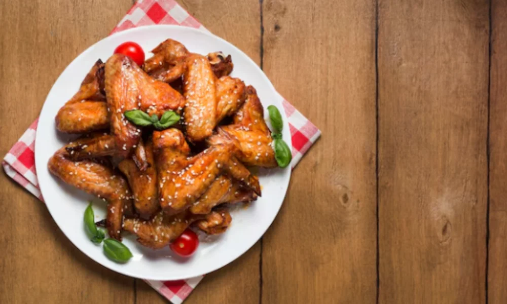 A plate of sesame-glazed chicken wings garnished with basil and cherry tomatoes