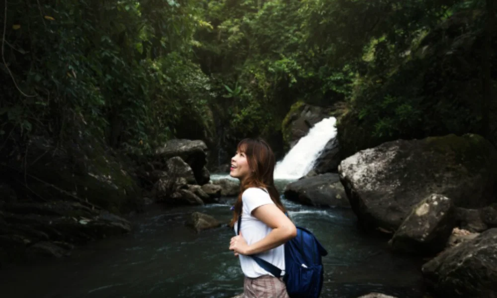 Woman with a backpack smiles while standing near a rocky stream surrounded by lush greenery-places to visit in el salvador