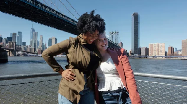 Two women stand smiling in front of the Brooklyn Bridge-new york city attractions map