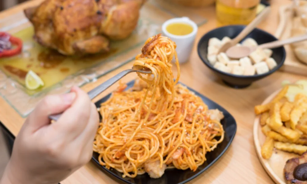 A hand twirls spaghetti with tomato sauce on a fork over a black plate-easy chicken spaghetti recipe