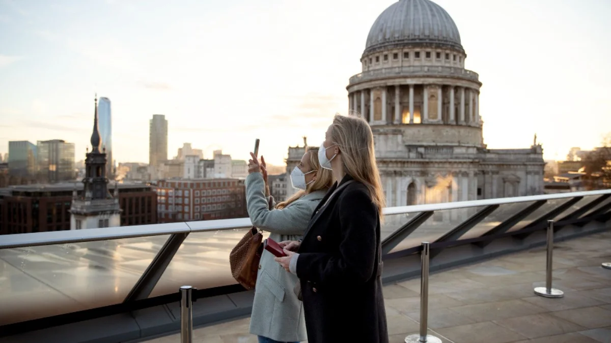 Two women wearing masks stand on a rooftop terrace