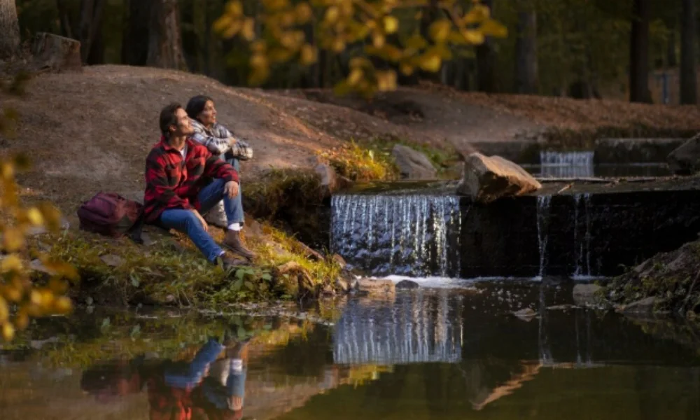 A couple sits by a serene forest stream with small waterfalls, surrounded by trees-washington dc travel guide
