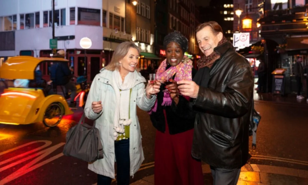 A joyful group of three people stands on a bustling city street at night