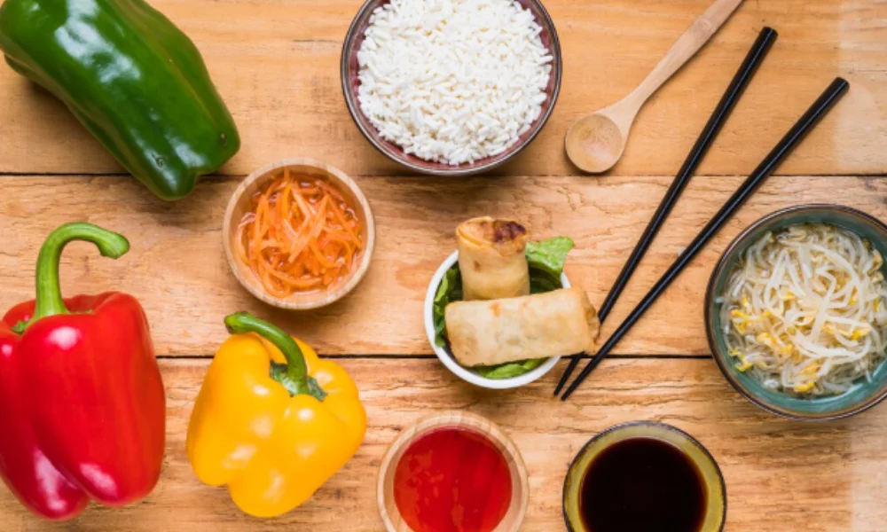 A colorful assortment of Asian ingredients on a wooden table includes green, red, and yellow bell peppers
