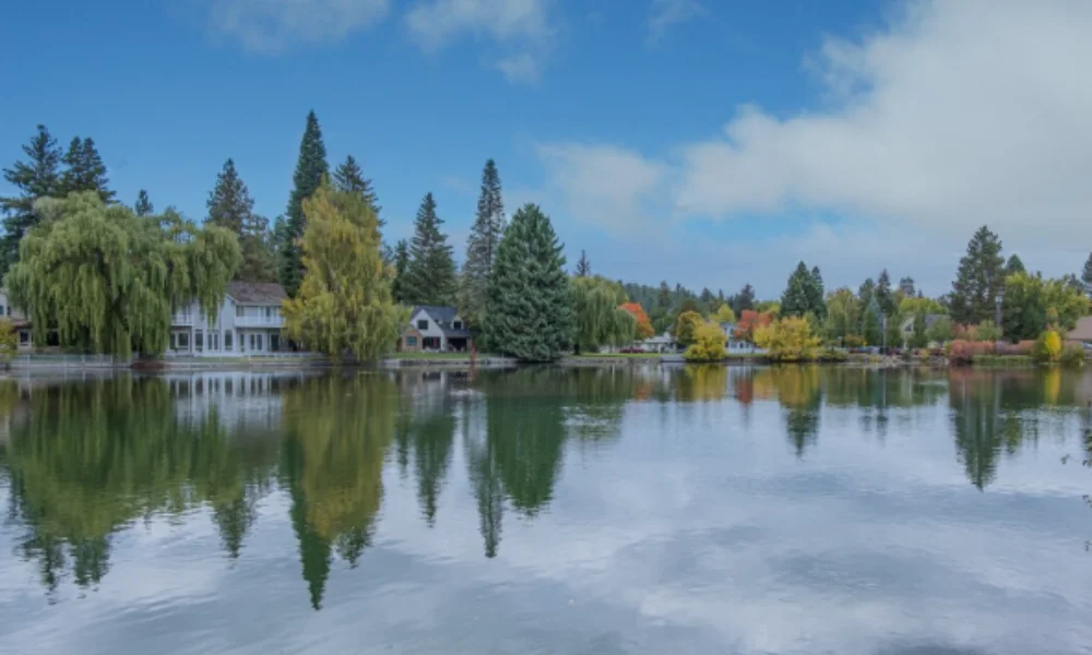 A tranquil lakeside scene with houses and lush trees reflected on the water