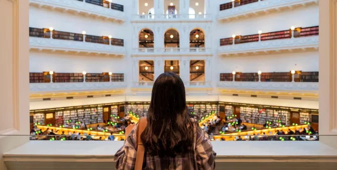 A woman gazes out of a window, observing a library