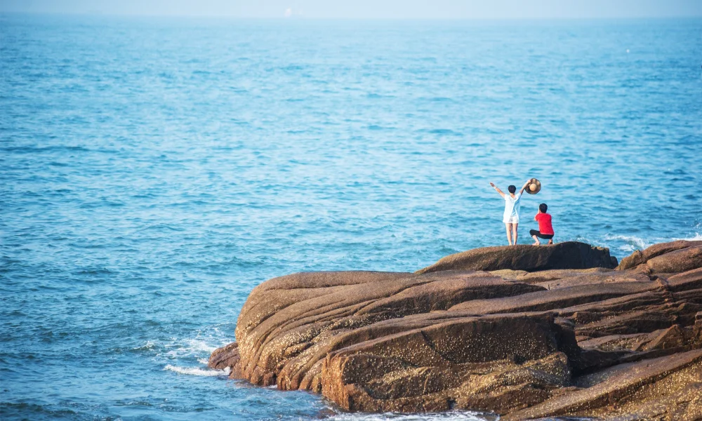 Two people on large coastal rocks by a calm blue sea