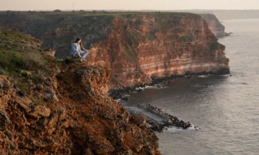 A person sits calmly on a rugged cliff edge overlooking the ocean-places to visit in france