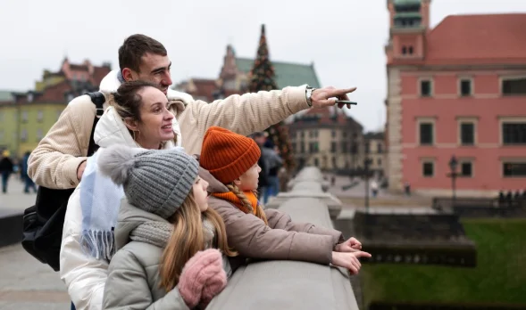A family of four, dressed warmly in jackets and knit hats, stands on a bridge-cheap travel destinations in Europe