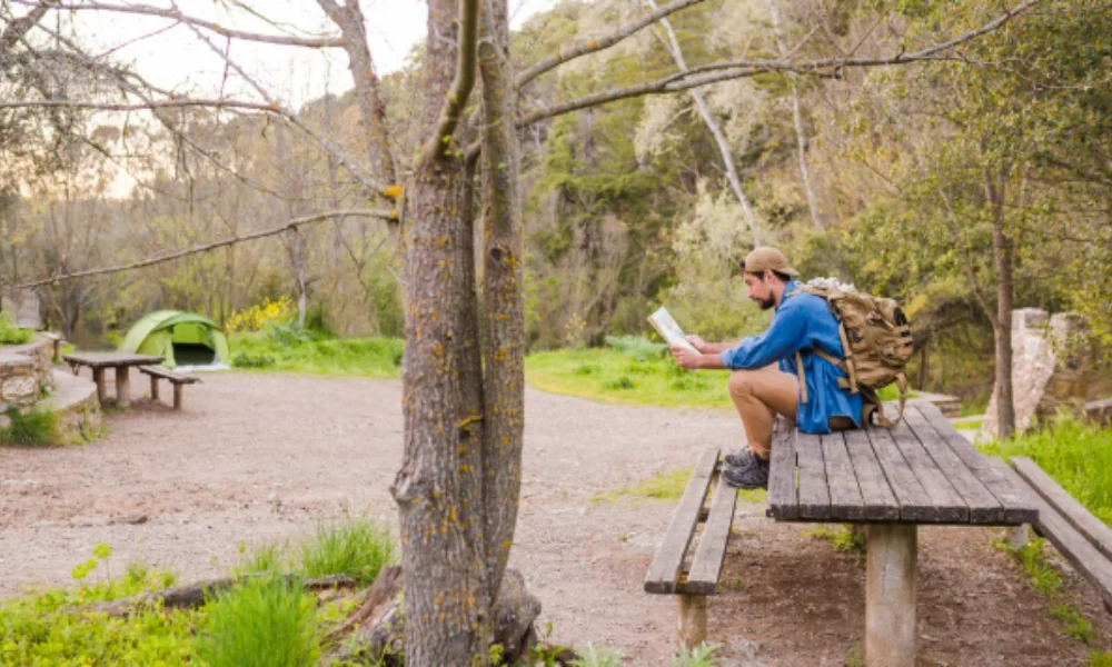 A man in outdoor gear reads a map while sitting on a picnic table in a forested campsite-places to visit in nashville
