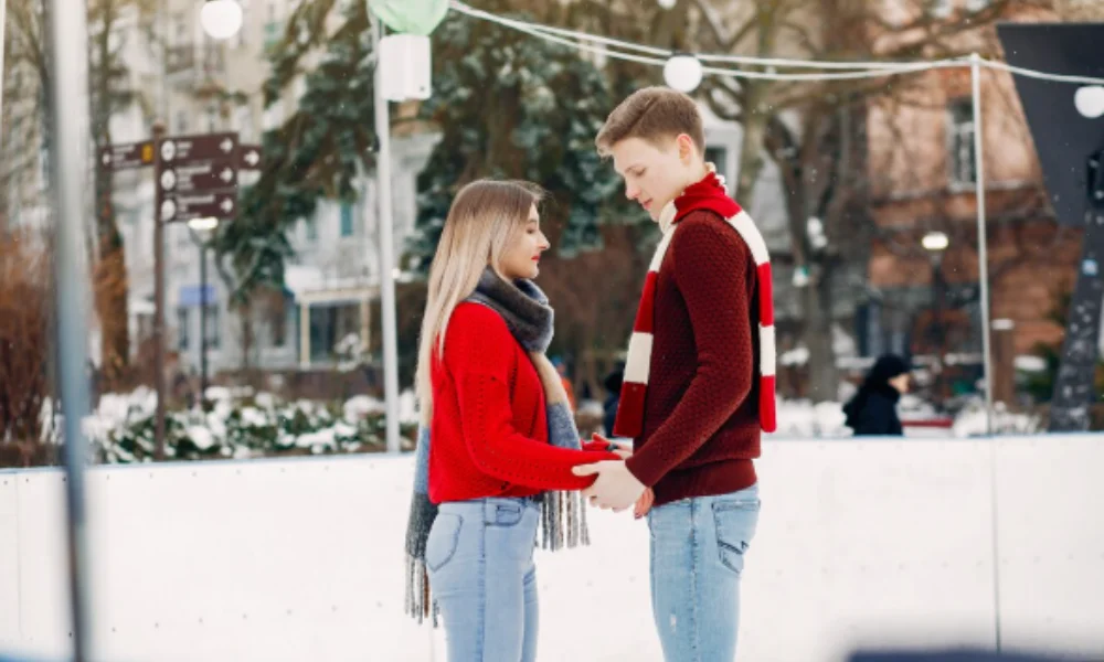 A young couple in red winter clothes hold hands on an ice rink