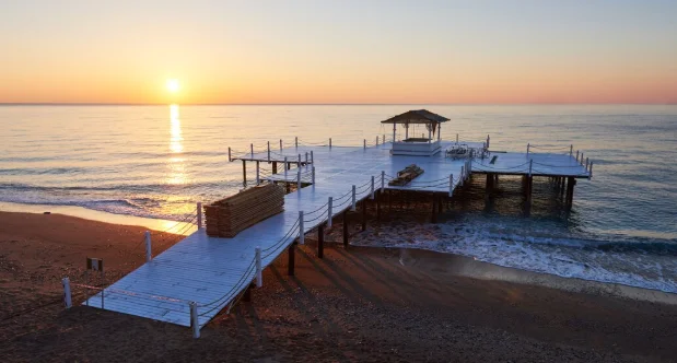 A serene sunrise over a calm ocean with a white wooden pier extending into the water