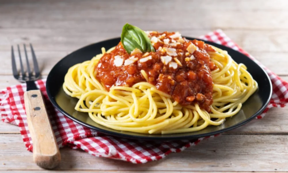 Plate of spaghetti topped with tomato sauce and a basil leaf on a wooden table-family easy dinner recipes